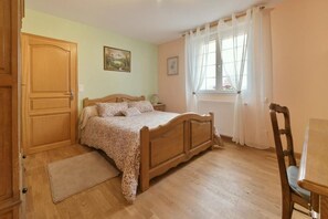 Um quarto com cama de madeira, guarda-roupa de madeira, janela com cortinas e uma cadeira de madeira.