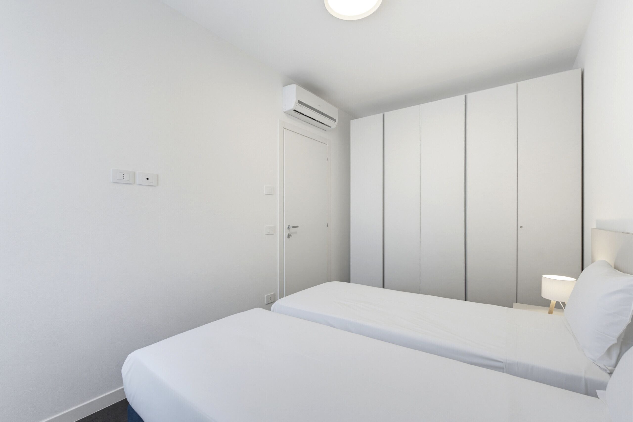 Una camera d'albergo dal design minimalista con un letto, un armadio e un condizionatore d'aria a parete.