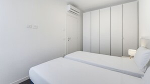 Minimalistinen hotellihuone, jossa on sänky, vaatekaappi ja seinälle asennettu ilmastointilaite.