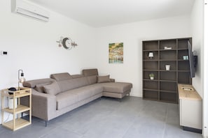 Ein modernes Wohnzimmer mit einer Eckcouch, einer Wanduhr, einem Gemälde und einer eingebauten TV-Konsole.