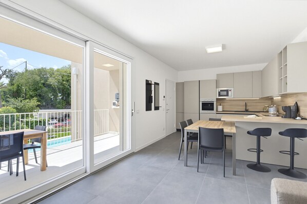 A modern kitchen with a dining area, a bar, and a sliding glass door leading to a balcony.