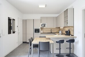 Una cucina compatta con zona pranzo, comprensiva di tavolo e sedie, e un piccolo bancone con sgabelli.