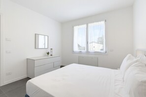 A minimalist bedroom with a bed, a dresser, a mirror, and a window.