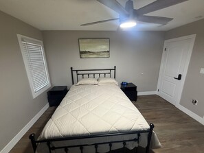 Ein Schlafzimmer mit einem Bett, einem Nachttisch, einem Deckenventilator, einer Wanduhr und einer Tür.