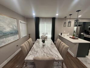 A modern dining area with a marble table, upholstered chairs, and a vase of flowers. - Luxury Executive Home 3BR/2BA Finished Basement Free Parking (Detroit)