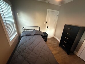 Ein Schlafzimmer mit einem Bett, einem Schminktisch, einer Tür und einem Fenster mit Jalousien.