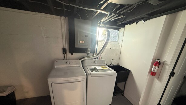 Ein Waschraum mit zwei weißen Waschmaschinen, einem schwarzen Waschbecken und einem an der Wand montierten Feuerlöscher.