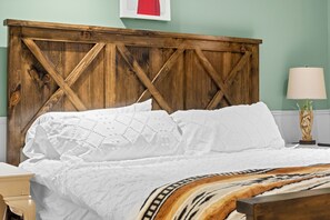 Cama com cabeceira de madeira, roupa de cama branca e manta estampada.