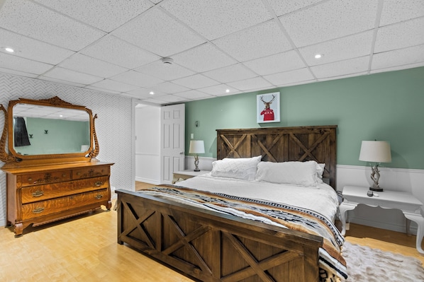 A bedroom with a wooden bed, a dresser, a mirror, and a wall with a picture.
