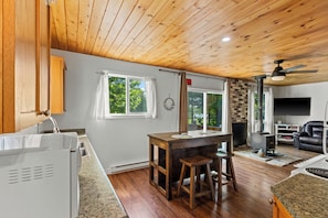 A modern kitchen with a wooden ceiling, a built-in stove, and a dining area with stools.