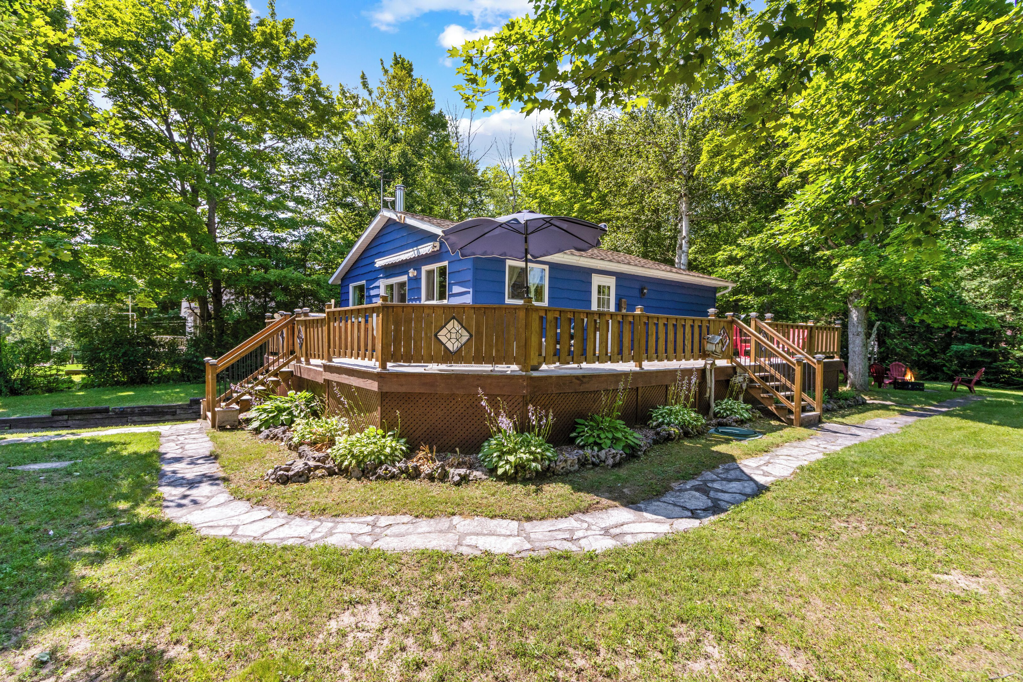 Une maison bleue avec une terrasse en bois, entourée de verdure et bordée d’un chemin de pierres.