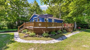 A blue house with a wooden deck, surrounded by greenery and a stone pathway.
