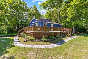 A blue house with a wooden deck, surrounded by greenery and a stone pathway.