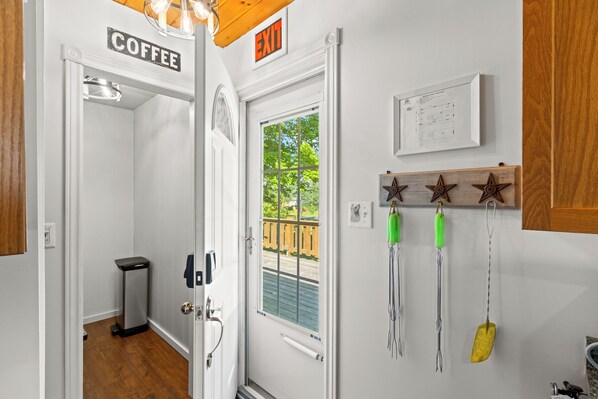 A hotel room with a coffee sign, an exit sign, a window with a view of greenery, and a wall-mounted light fixture.