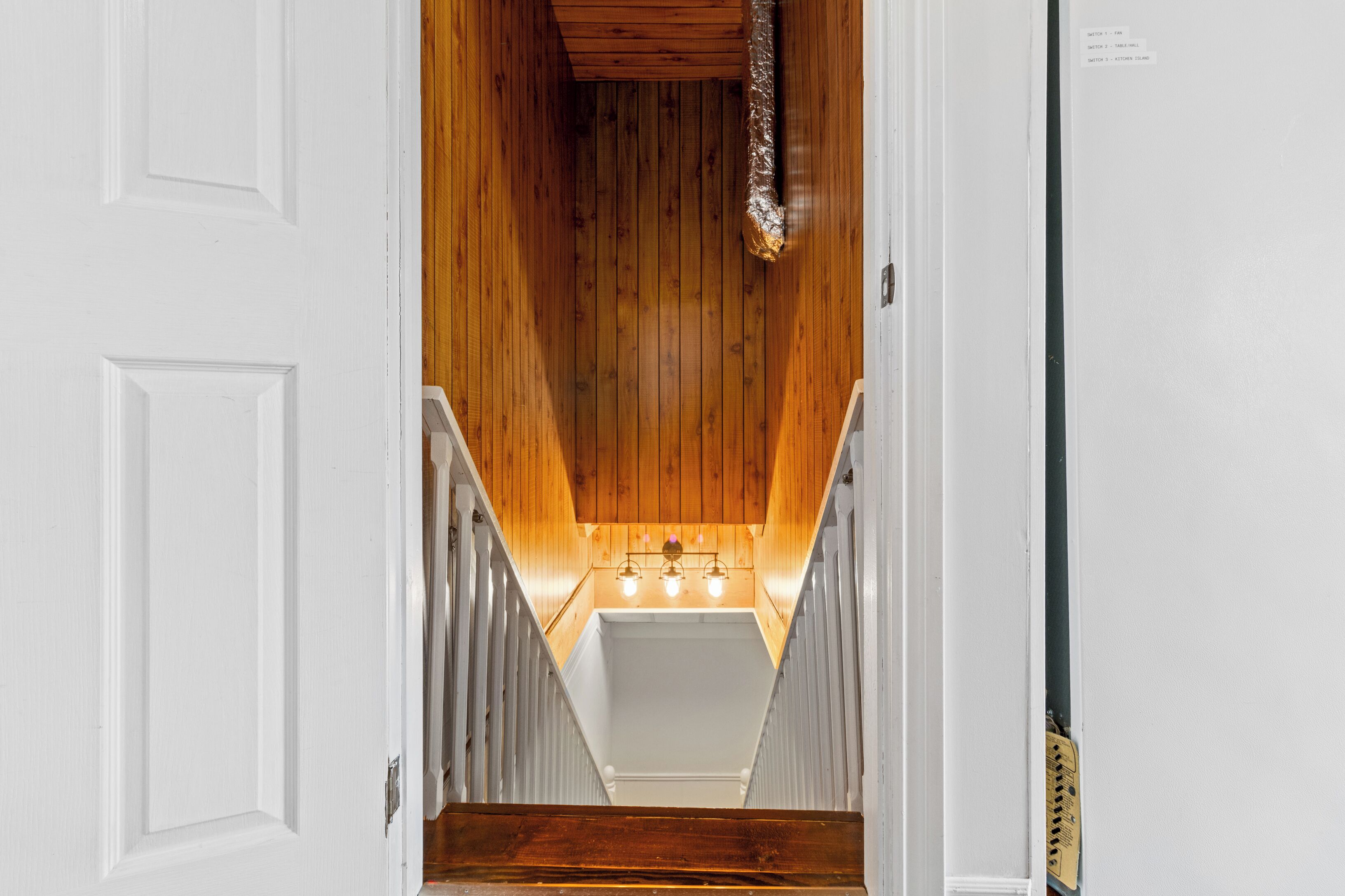 Un escalier en bois, avec une porte blanche en haut et un luminaire en bas.
