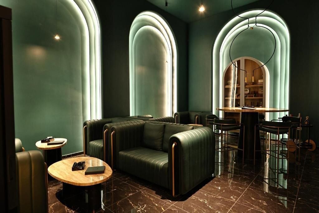 A modern lounge area with leather sofas, a round wooden table, and a bar area with stools.