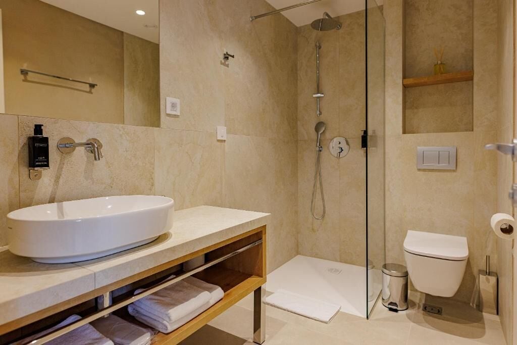 A modern bathroom with a large white sink, a glass-enclosed shower, and a toilet.
