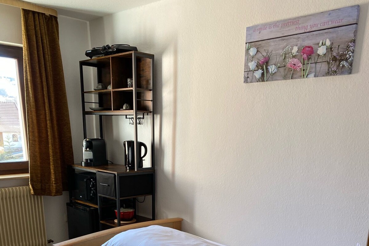 A single bed with a wooden frame and white bedding in a room with a radiator, a shelf with various items, and a wall-mounted picture.