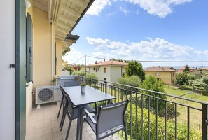 A balcony with a table and chairs, an air conditioning unit, and a view of neighboring houses. - Regarda - Basiliko Cosy Apartment with pool, pets allowed (Lazise)