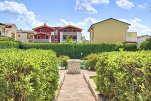 A residential area with a paved pathway leading to a stone fountain, surrounded by well-maintained hedges. - Regarda - Basiliko Cosy Apartment with pool, pets allowed (Lazise)