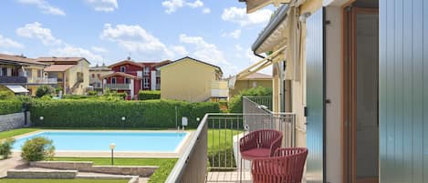 A residential property with a swimming pool, a covered patio with chairs, and a view of neighboring houses.