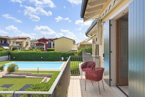 A residential property with a swimming pool, a covered patio with chairs, and a view of neighboring houses. - Regarda - Basiliko Cosy Apartment with pool, pets allowed (Lazise)