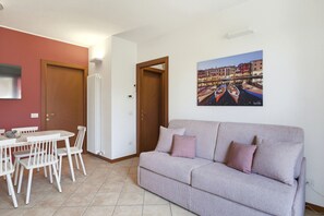 Ein Wohnzimmer mit einer Couch, einem Esstisch mit Stühlen, einem Heizkörper und einem Bild einer Kanalansicht.