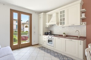 A compact kitchen with white cabinets, a gas stove, an oven, and a sink. - Regarda - Basiliko Cosy Apartment with pool, pets allowed (Lazise)