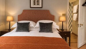 Habitación de hotel con cama, dos lámparas de noche, un cuadro en la pared y una puerta a cuadros.