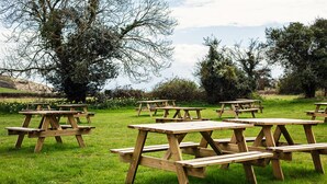 A picnic area with multiple wooden picnic tables arranged on a grassy field. - Super King/Twin Room at The Weld Arms (Wareham)