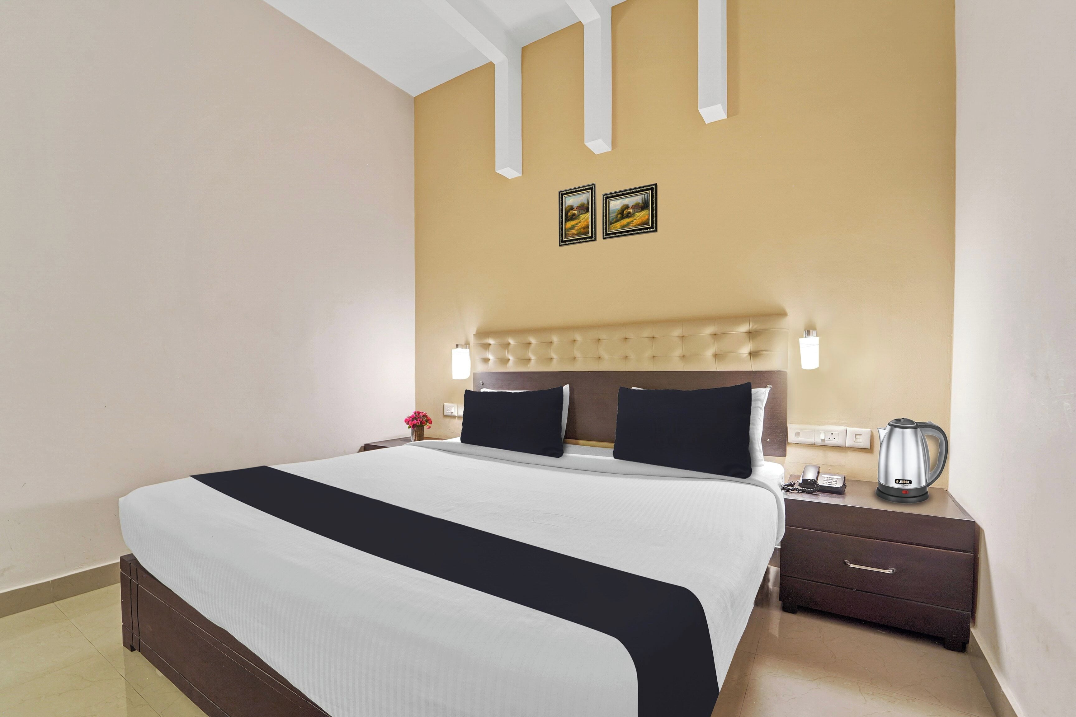 Habitación de hotel con una cama grande, una mesita de noche con lámpara, teléfono y tetera.