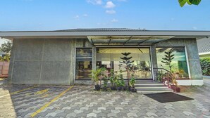 Un edificio moderno con tetto piano, ampie finestre e un'area d'ingresso pavimentata con piante in vaso.