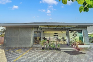 A modern building with a flat roof, large windows, and a paved entrance area with potted plants.