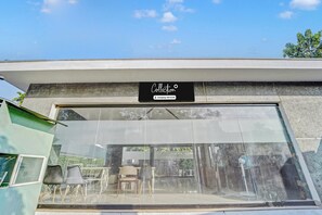 A building with a large glass facade, a sign reading 'Collection Company Serviced', and outdoor seating visible through the glass. - Collection O Kalady Near Airport (Aluva)
