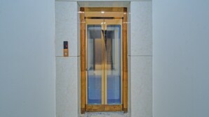 An elevator with a glass door, a control panel on the wall, and a wooden frame around the door. - Super Collection O Hyderabad Central (Hyderabad)