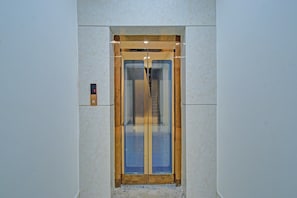 Hissi, jossa on lasiovi, seinässä oleva ohjauspaneeli ja oven ympärillä oleva puukehys.
