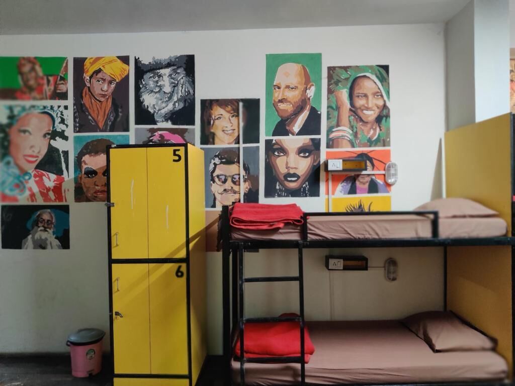 A dormitory room with bunk beds, a yellow locker, and a wall decorated with various portraits.