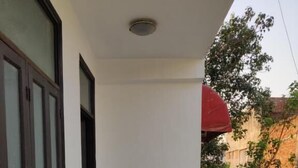 A narrow balcony with a metal railing, a red umbrella, and a view of a building with trees. - Heistel Delhi (New Delhi)
