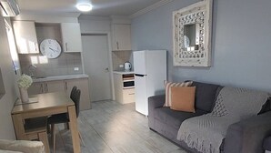 A modern living space with a dining area, kitchenette, and a sofa with a decorative mirror. - Tidy one bedroom apartment (Leeton)
