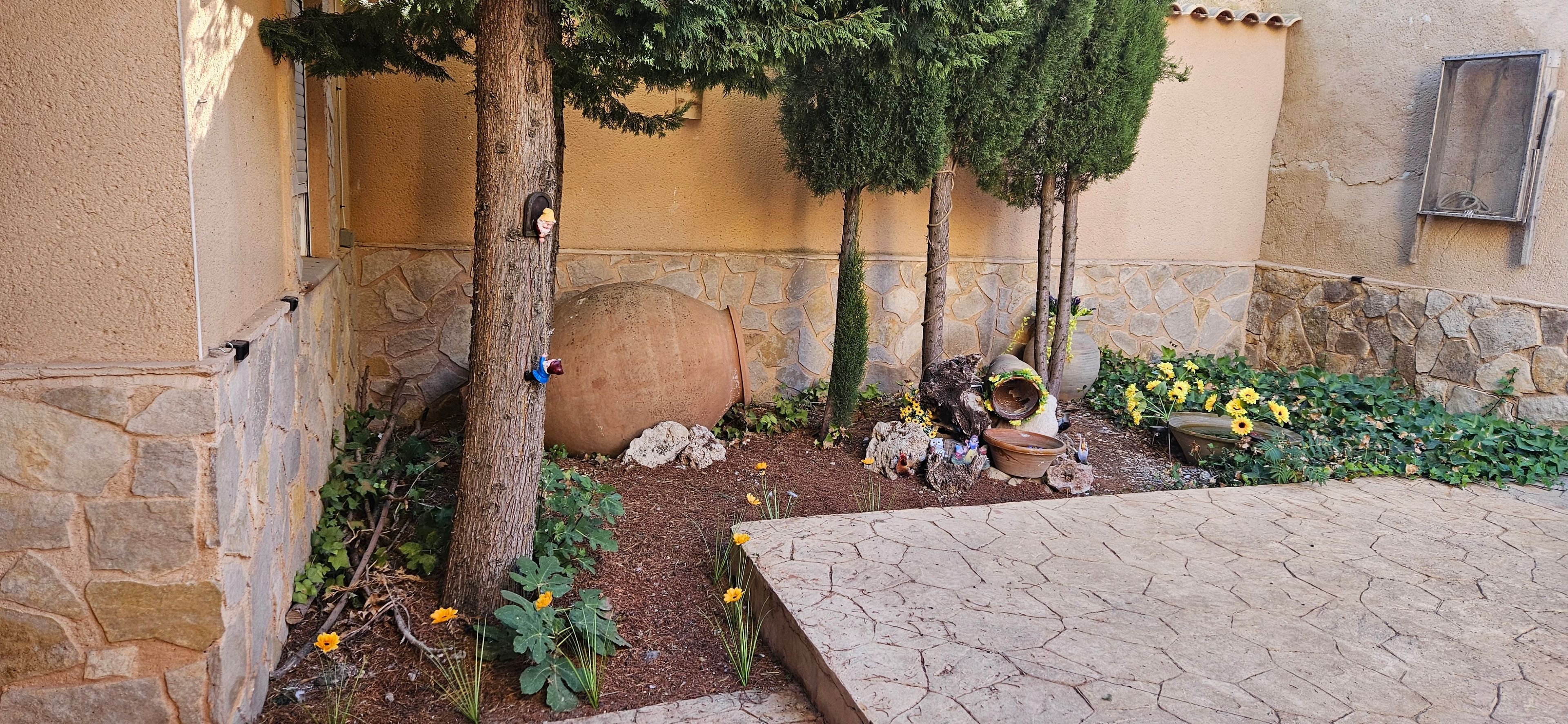 Un patio con paredes de piedra, suelo de baldosas y una variedad de plantas y flores.