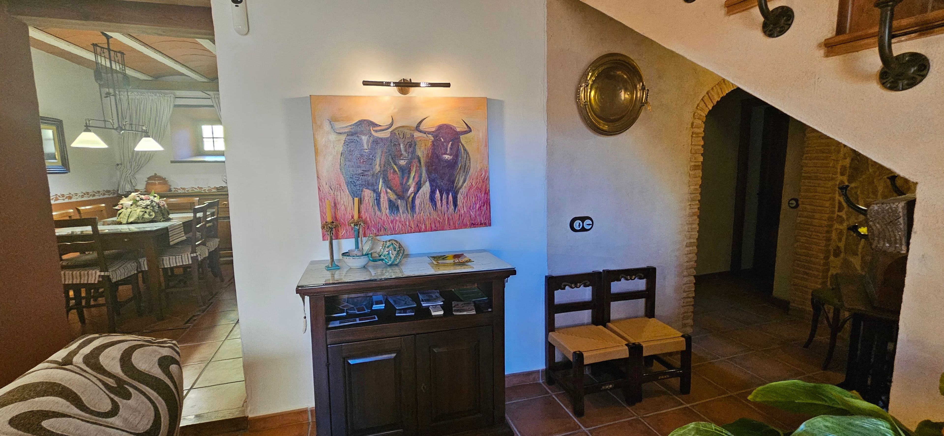 Un comedor con una mesa dispuesta para dos, un cuadro en la pared y un mueble bajo con objetos encima.