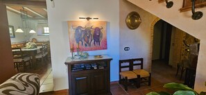 Zona de menjador amb una taula preparada per a dues persones, un quadre penjat a la paret i un petit armari amb objectes a sobre.