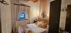 A bedroom with a bed, curtains, a nightstand, a wall-mounted lamp, and a window.