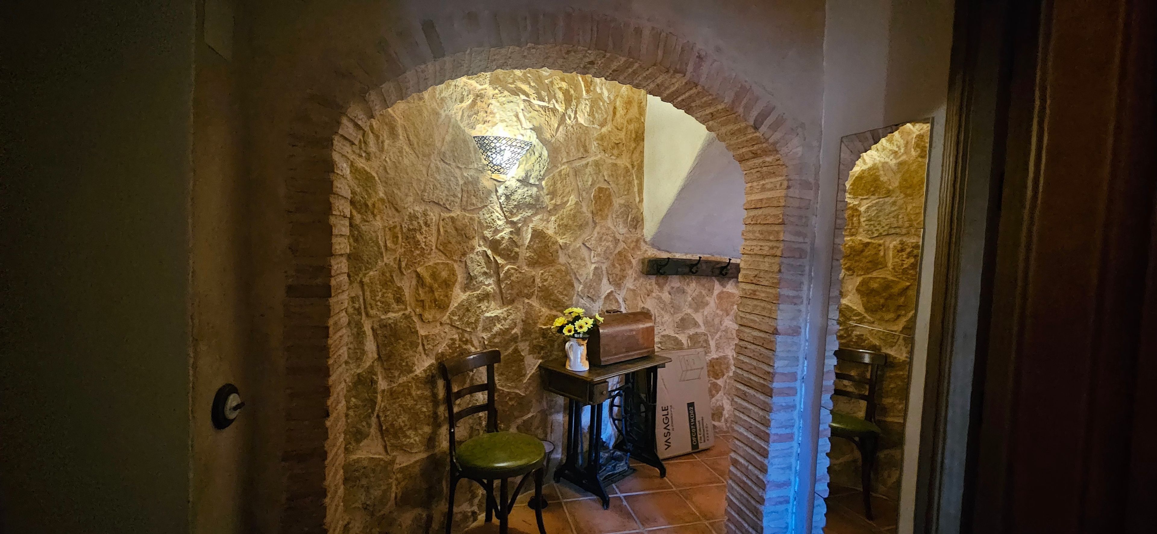 Un arc en pierre mène à une pièce où se trouvent une table, des chaises et un vase rempli de fleurs.