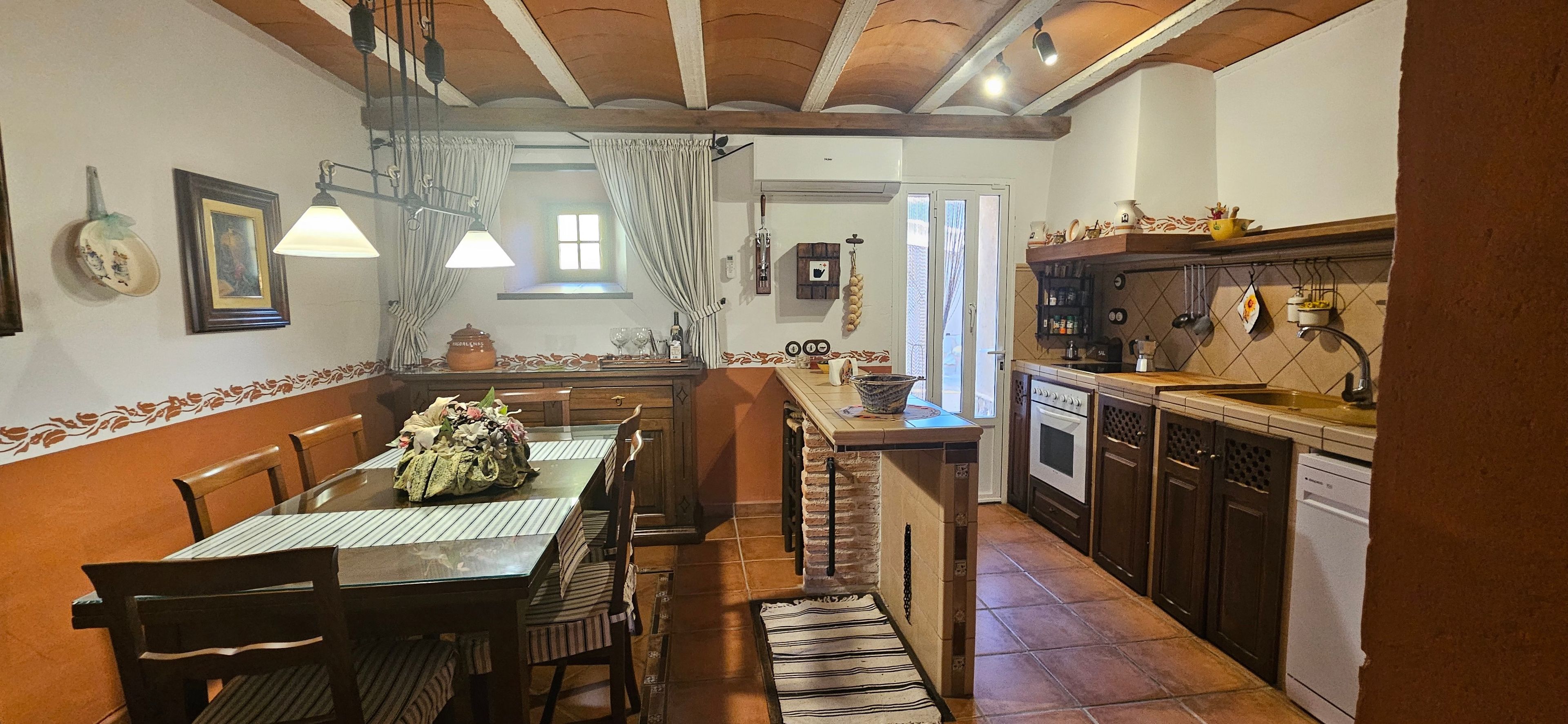 A dining area with a wooden table and chairs, a kitchen with a stove and cabinets, and a window with curtains.