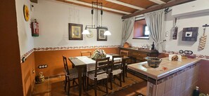 Un comedor con una mesa dispuesta para cuatro, una cocina con ventana y una lámpara colgante.