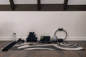 Eine Yogamatte, Hanteln, eine Wasserflasche, eine Pflanze, ein Yoga-Block und ein Widerstandsband auf Holzboden.