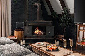 Ein gemütliches Wohnzimmer mit Kaminofen, einer Couch, einem Couchtisch mit Snacks und einer Pflanze.