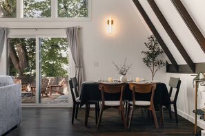 A dining area with a table set for four, a potted plant, and a wall-mounted light fixture. - Luxury A-Frames - Pet-Friendly - Fenced Yard - Sleeps 12 - Minutes to Greenway! (Asheville)