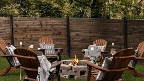 A fire pit surrounded by Adirondack chairs with blankets and candles, set against a wooden fence. - Luxury A-Frames - Pet-Friendly - Fenced Yard - Sleeps 12 - Minutes to Greenway! (Asheville)